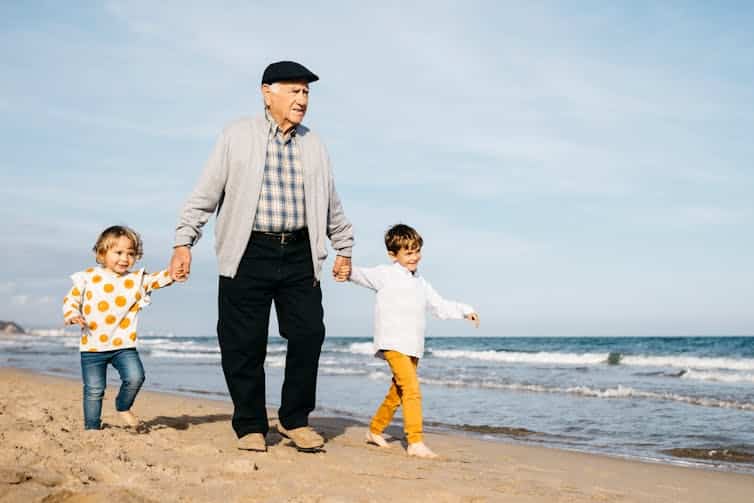 Grandfather strolling with his grandchildren hand in hand on the beach.