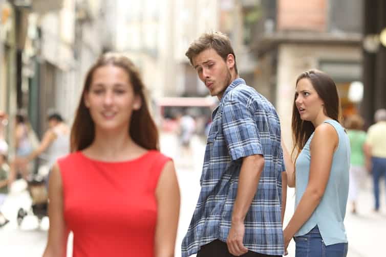 Young man ogles an attractive woman over his shoulder as his girlfriend looks annoyed.